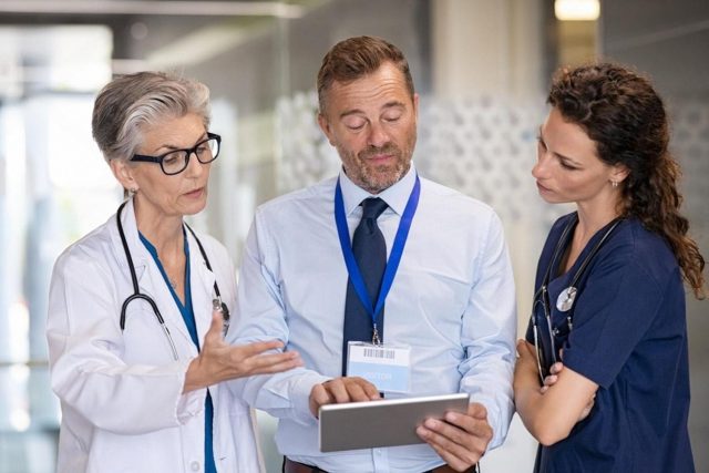 Two doctors and a hospital administrator reviewing a patient queue on a tablet in a UAE clinic corridor